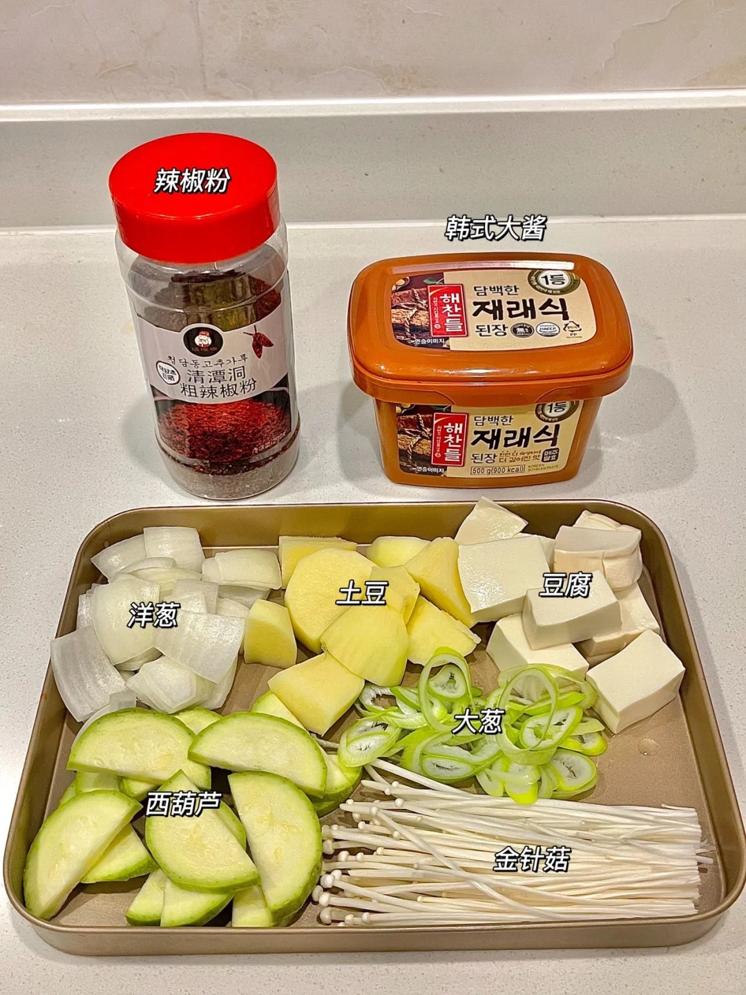整齐摆放的食材：洋葱、土豆、豆腐、大葱、西葫芦、金针菇，以及辣椒粉和韩式大酱
